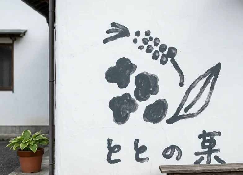 白壁に描かれた手描き風の「ととの菓」ロゴ。麹や葉をモチーフにしたイラスト入り